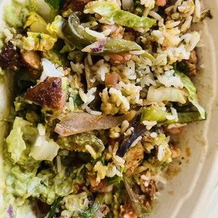 Bowl consisting of lettuce, white cilantro rice, chicken, green peppers, guacamole, picó de gayo, and red salsa.