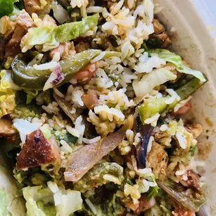 Bowl consisting of lettuce, white cilantro rice, chicken, green peppers, guacamole, picó de gayo, and red salsa.