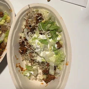 A bowl with brown rice, beans, Al pastor, sour cream, cheese  and lettuce.