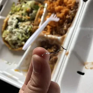a hand holding a fork in front of a tray of food