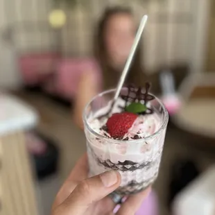 a hand holding a cup of chocolate and strawberries