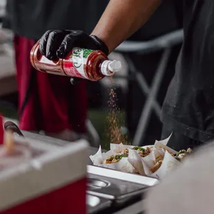 a person pouring ketchup onto a plate of food
