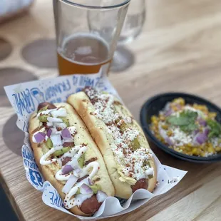 two hotdogs with toppings and a glass of beer