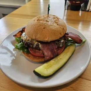 Bacon cheeseburger on gluten-free bun and a pickle spear.