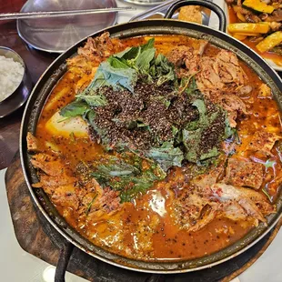 Gamjatang-jeongol spicy pork bone soup in a hot pot with potatoes, cabbage, perilla seeds.