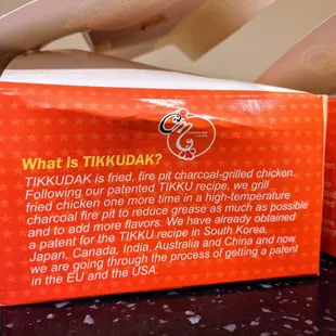 Side view of Choong Man Chicken fried chicken box. Description of Tikkudak (fried then baked chicken).