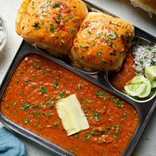 Pav Bhaji features a rich and flavorful vegetable curry made with mashed potatoes, tomatoes, peas, carrot, and a blend of aromatic spices.