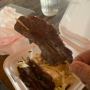 a hand holding a skewer of meat