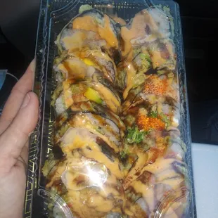 a hand holding a plastic tray of sushi