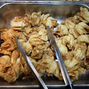 a bowl of fried dumplings with tongs