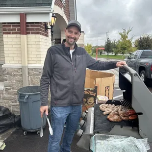 Jon is grilling up hot dogs and bratwursts to serve with sodas and potato chips.