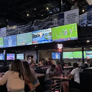 a group of people sitting at a bar watching televisions