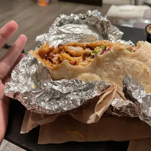 a person&apos;s hand holding a taco wrapped in foil