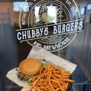 a hand holding a burger and fries