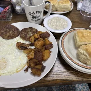 Breakfast combo: eggs, sausage patties, home fries, biscuits and gravy with coffee.