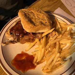 Grilled chicken sandwich with western chicken topping of bbq, bacon and an onion ring, with a side of fries.