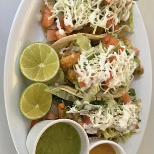 a plate of tacos with sauce and lime wedges