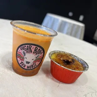 a cup of orange juice next to a container of creme