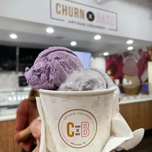 Side view of a triple scoop: ube coconut crunch, lavender honey, and black sesame on the bottom