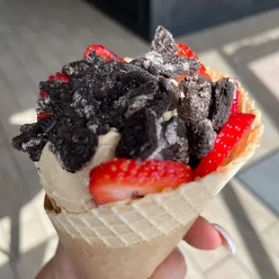 a hand holding a cone of ice cream with chocolate and strawberries