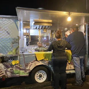 a man and a woman ordering food from a cart