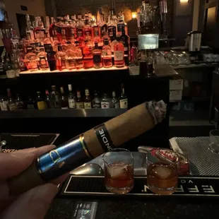 a hand holding a cigar and two shot glasses