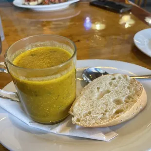 a cup of soup and a piece of bread on a plate