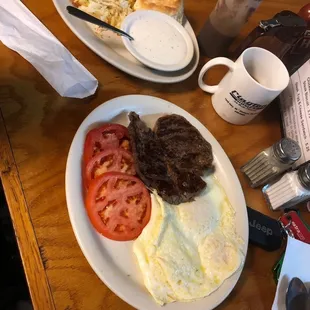 Three eggs and 6oz ribeye with tomatoes , biscuits and gravy with hash browns