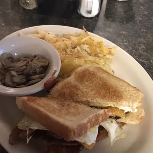 Bacon, egg, and cheddar cheese sandwich with a side of grilled mushrooms, and an order of hashbrowns.