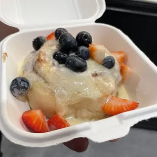 Cinnamon roll with crème brûlée frosting topped with fresh strawberries and blueberries