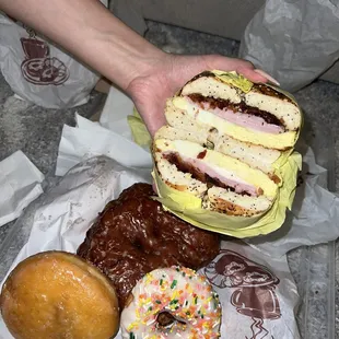 a person holding a sandwich and various donuts
