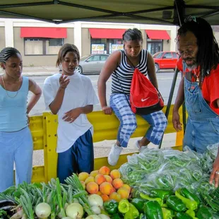 a group of people standing around a fruit stand