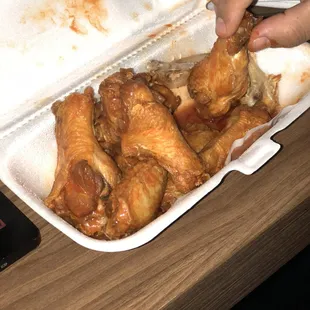 a person putting a piece of chicken in a styrofoam container
