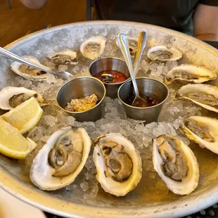 a platter of oysters with dipping sauce and lemon wedges