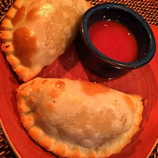 two empanadas on a plate with dipping sauce
