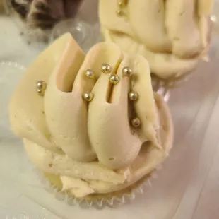 two cupcakes with white frosting and gold decorations