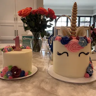 A small cake with flowers next to a larger floral unicorn themed cake