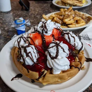 a waffle with whipped cream, strawberries, and chocolate syrup