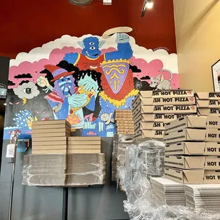 a stack of pizza boxes in front of a mural