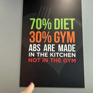 a hand pointing at a sign that reads 70 % diet 30 % gym abs are made in the kitchen not in the