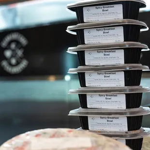 a stack of six takeout containers with a pizza in the background