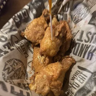 a basket of fried chicken with sauce being drizzled over it