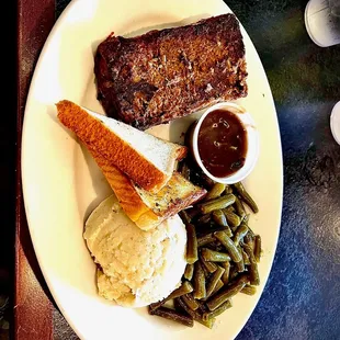 a plate of meat, mashed potatoes, and green beans