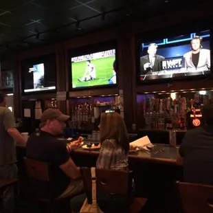 people sitting at a bar watching tvs