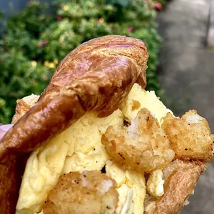 a hand holding a croissant sandwich