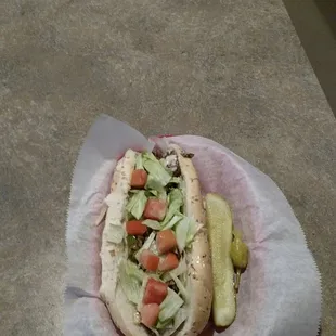 a hot dog with lettuce, tomatoes, and pickles