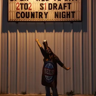 a man holding a beer in front of a sign