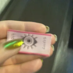 a person&apos;s hand holding a small pink box with an eye drawn on it