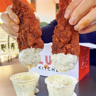 two hands holding fried chicken strips