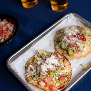 two glasses of beer and a tray of food